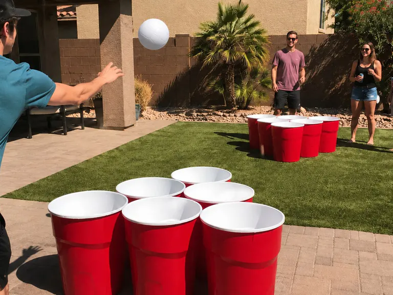 Giant yard pong rental game with two opposing sets of six red cups and a white volleyball in a Mesa backyard