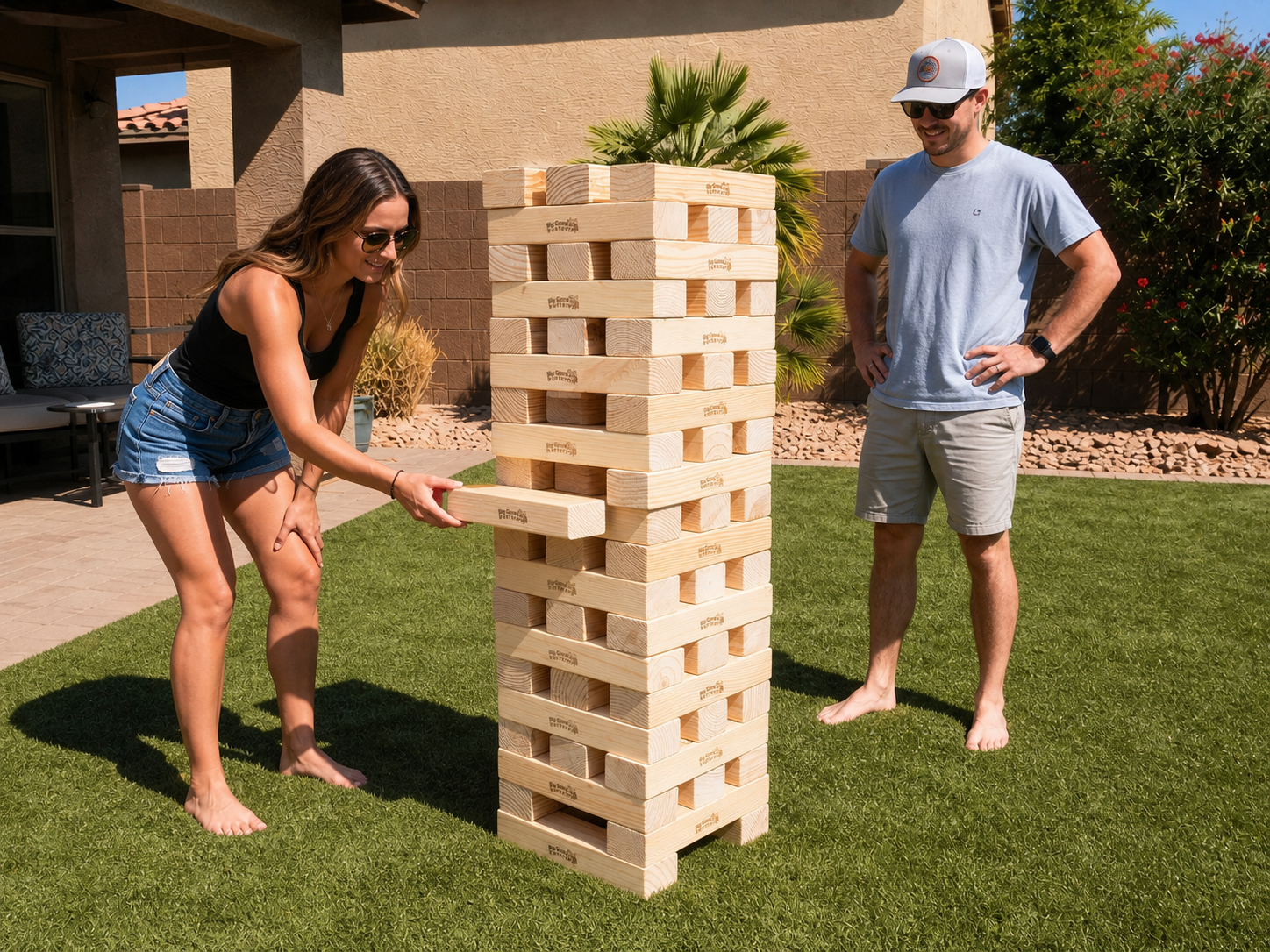 Two adults playing Giant Jenga on a sunny Arizona backyard lawn