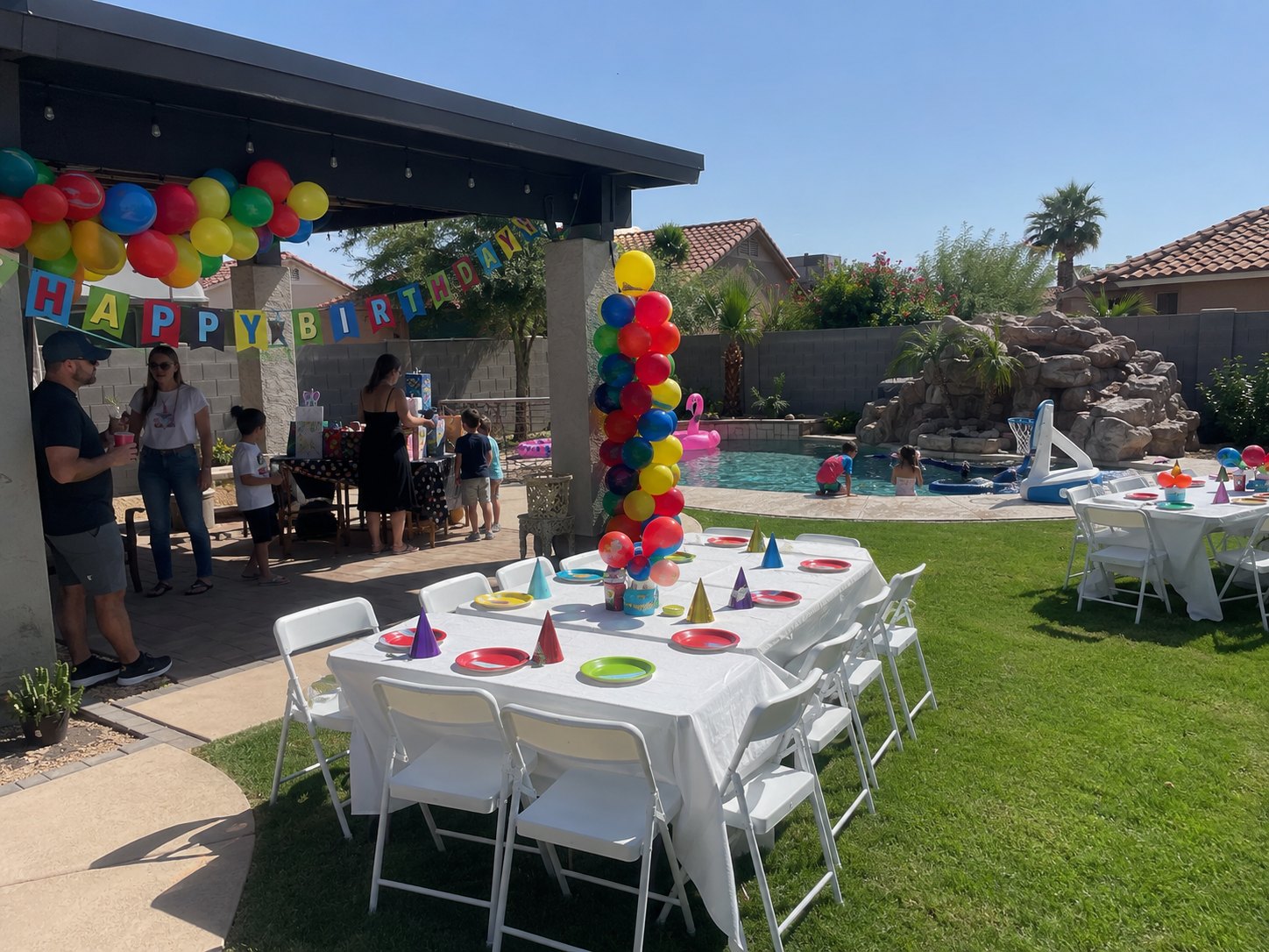 Arizona backyard birthday pool party with white folding chairs, guest tables, colorful balloons, and a Happy Birthday banner